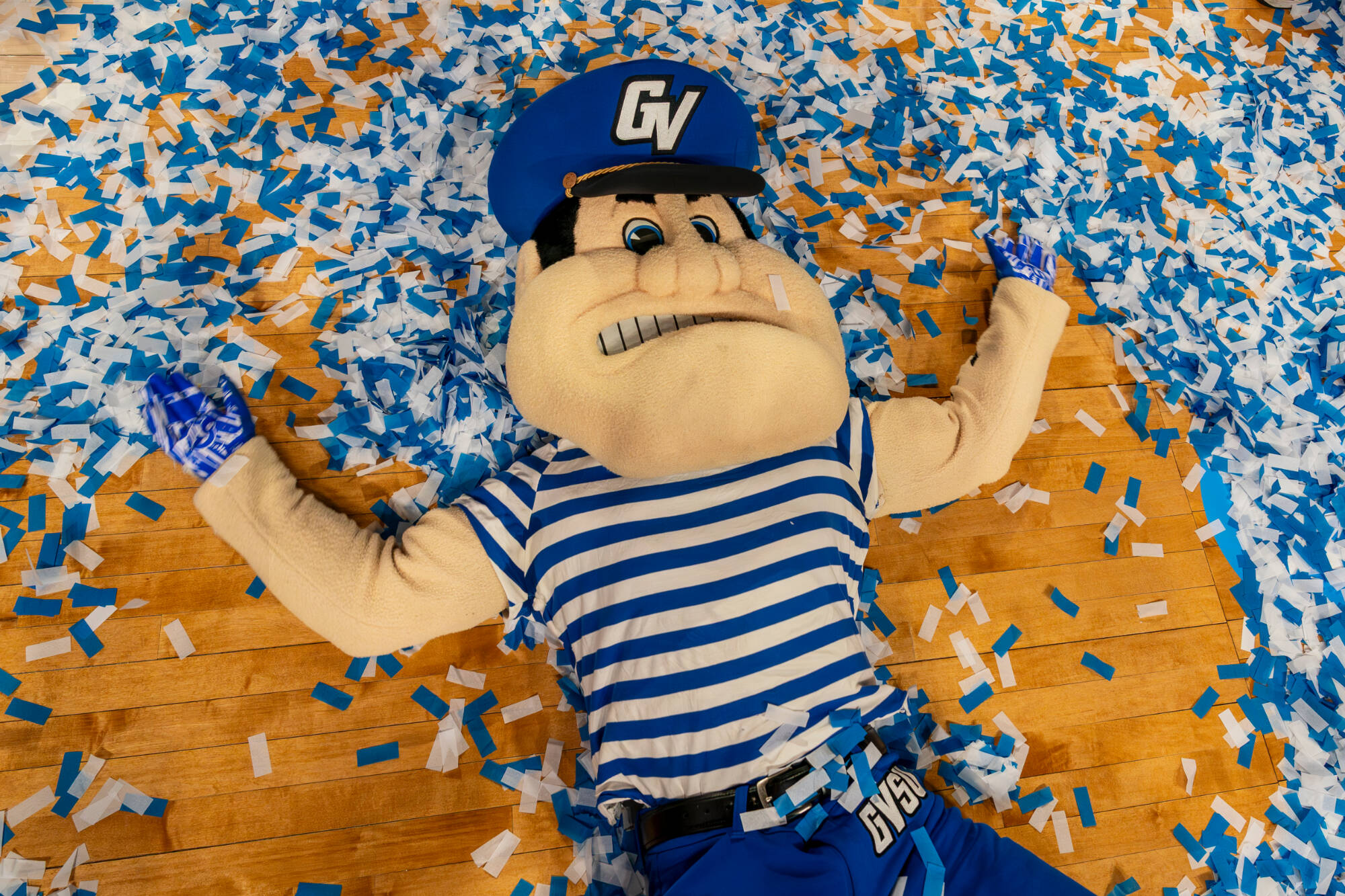 Louie the Laker laying in a pile of confetti on a basketball court